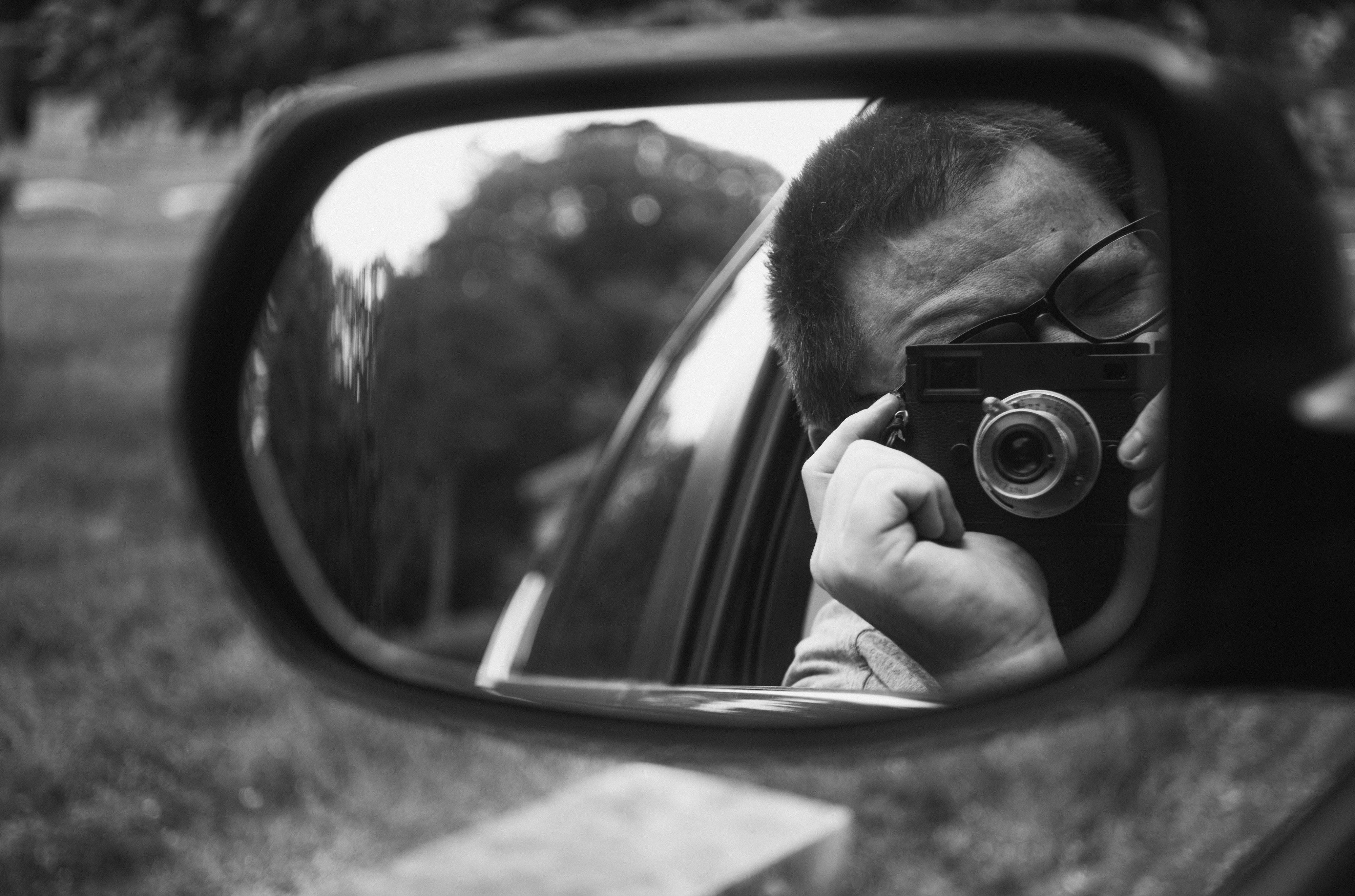 Một bức ảnh đen trắng được chụp bằng Leica M10 Monochrom hiển thị máy ảnh và nhiếp ảnh gia trong gương chiếu bên.